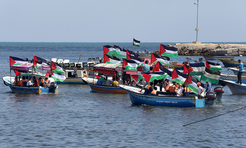 Palestinians hold their national flag to show support for activists aboard a flotilla of boats who are soon to set sail for Gaza at the seaport of Gaza City on June 24, 2015 (AFP Photo)
