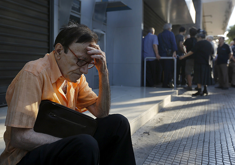 Giorgos, a 77-year-old pensioner from Athens, sits outside a branch of the National Bank of Greece as he waits along with dozens of other pensioners, hoping to get their pensions in Athens, Greece June 29, 2015 (Reuters Photo)