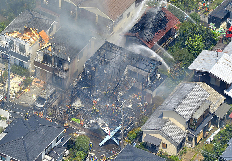 Firefighters investigate the site of a plane crash in the suburbs of Tokyo, Sunday, July 26, 2015. (Kyodo News via AP)