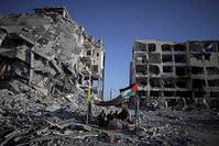 A Gazan family sits in a shelter made of a blanket stretched over four boles next to their home that was destroyed by Israeli airstrikes last summer.