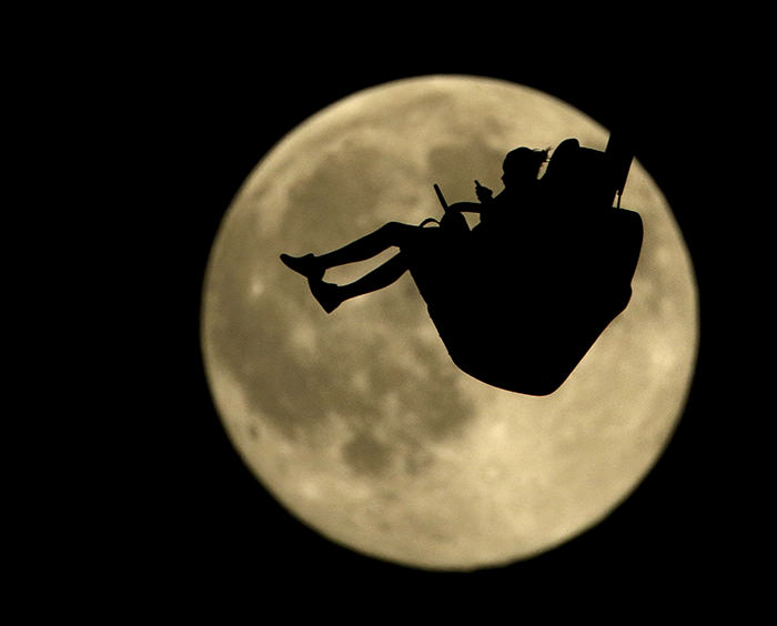 A girl is silhouetted against a rising full moon as she ride an attraction at Worlds of Fun amusement park Thursday, July 30, 2015, in Kansas City (AP Photo)