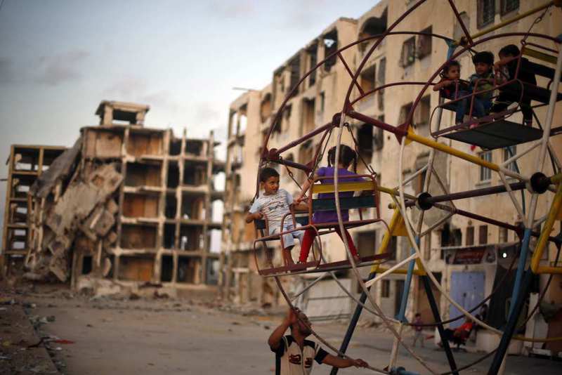Palestinian children enjoy a ride on a ferris wheel near residential buildings destroyed by Israeli bombs in Gaza.