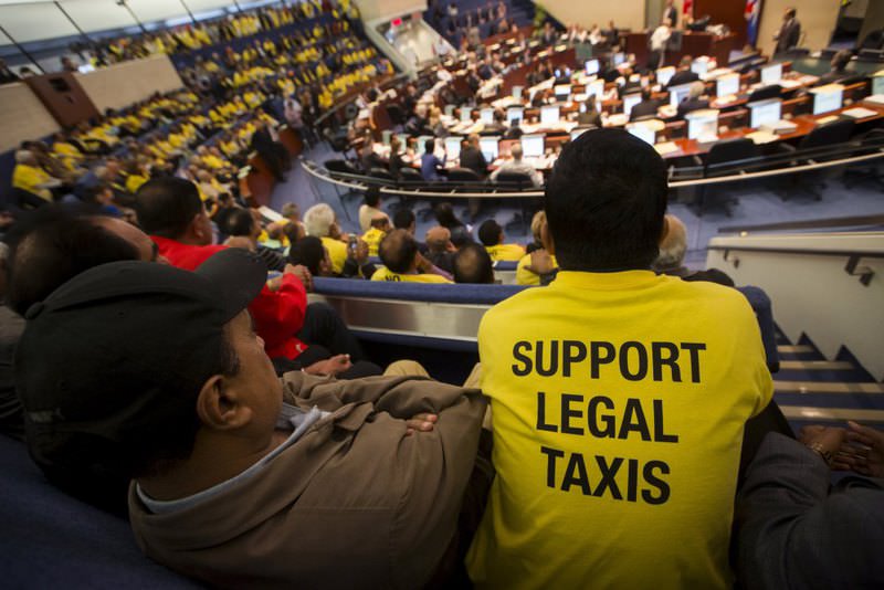 Uber protesters in yellow shirts listen to the Toronto city council debate over new taxi regulations.