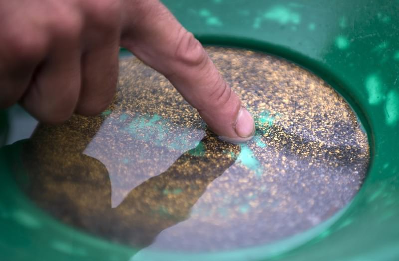A man pointing to pieces of alluvial gold in a pan of sand from the Tundzha River near Kazanlak, central Bulgaria.