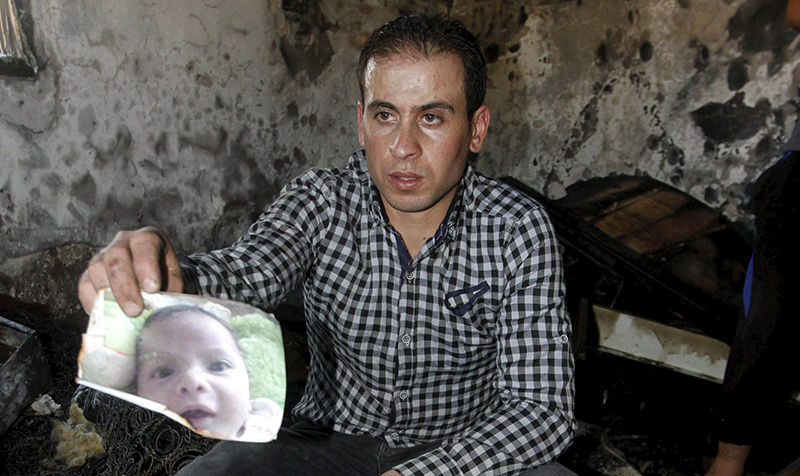 A relative of 18-month-old Palestinian baby Ali Dawabsheh, who was killed after his family's house was set to fire in a suspected attack by Jewish extremists, shows his picture at the burnt house (Reuters Photo)