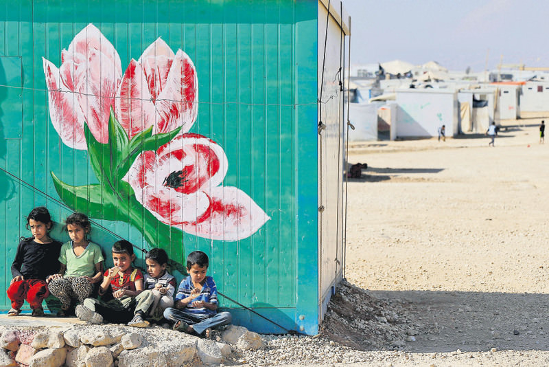 A group of Syrian refugees posing in front of their family's painted caravan at Al Zaatari refugee camp, in Mafraq city of Jordan near the border with Syria