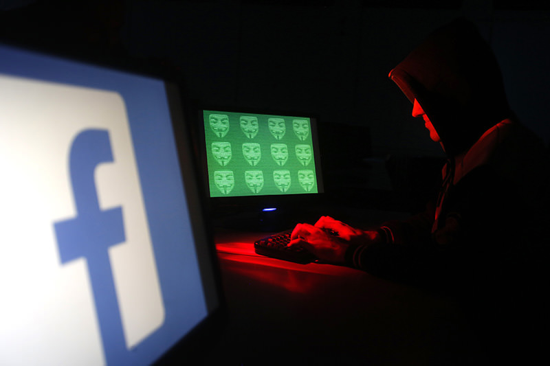 Man poses in front of on a display showing a Facebook logo and the word 'cyber' in binary code, in this picture illustration taken in Zenica December 27, 2014 (Reuters Photo)
