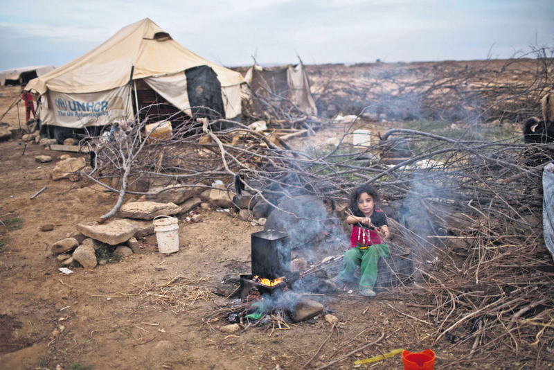 Syrian refugee Aysha Elwan, 5, helps her mother break wood to add to the fire to boil water outside her family's tent at an informal tent settlement on the outskirts of Mafraq, Jordan.