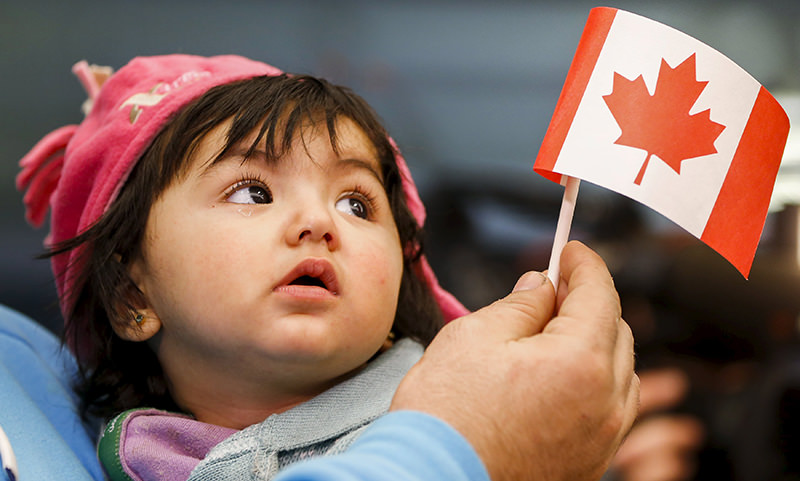 A young Syrian refugee looks up as her father holds her and a Canadian flag at the as they arrive at Pearson Toronto International Airport in Mississauga, Ontario (Reuters Photo)