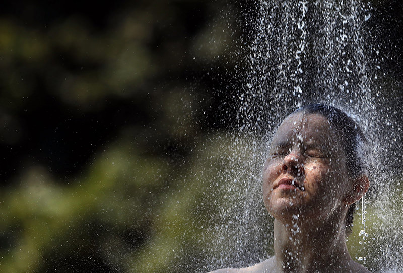 A girl takes a cold shower in order to refresh herself at Ada Ciganlija lake in Belgrade, Serbia, Tuesday, July 7, 2015. (AP Photo)