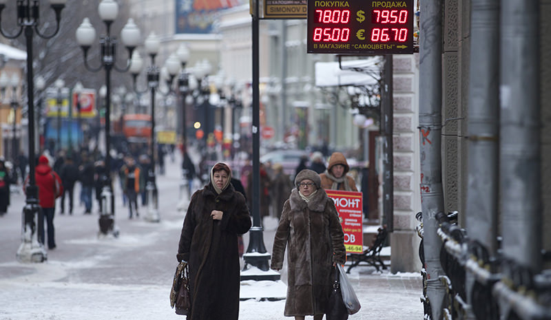People walk at a street passing an exchange booth in Moscow, Russia, Monday, Jan. 18, 2016 (AP Photo)
