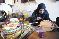 Cheynoune Zeineb, a Tuareg and imzad instrument maker, sits crossed legged while decorating an imzad with personalised Tuareg motifs in Tamanrasset in southern Algeria.