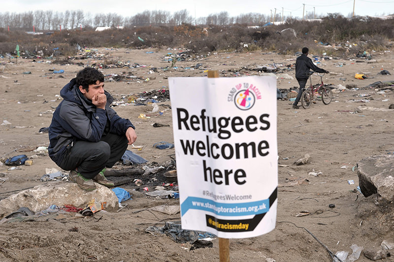 A migrant stands next to a banner on January 23, 2016 in the French port city of Calais, northern France (AFP)