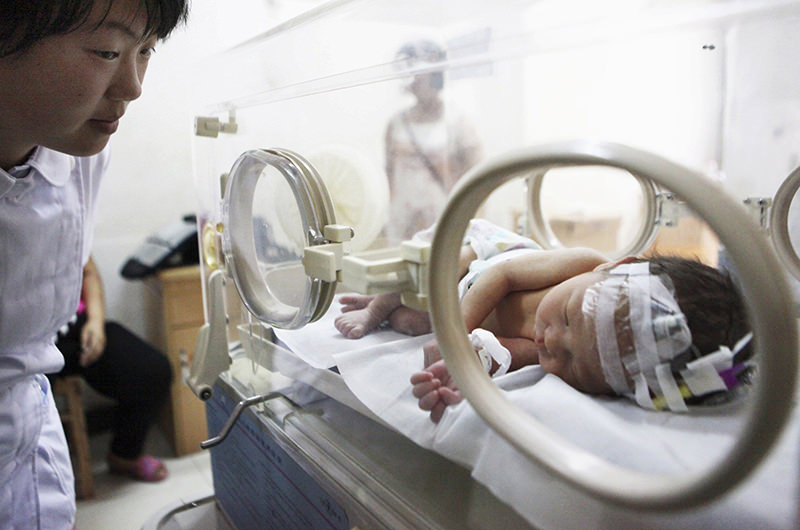 A nurse (L) looks at an abandoned newborn baby resting in an incubator after he was rescued from a sewage pipe at a hospital in Jinhua, Zhejiang province May 28, 2013 (Reuters Photo)