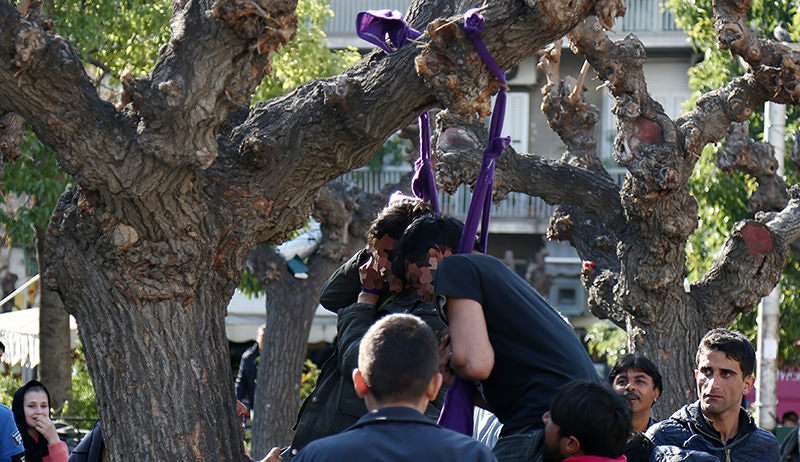 People rush to cut down two refugees who tried to commit suicide by hanging themselves with twisted lengths of fabric from a tree in central Athens' Victoria Square on Thursday, Feb. 25, 2016