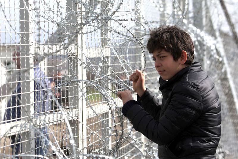 A boy yesterday looks through the barbed wire as migrants and refugees wait to cross the Greece-Macedonia border near the village of Idomeni.
