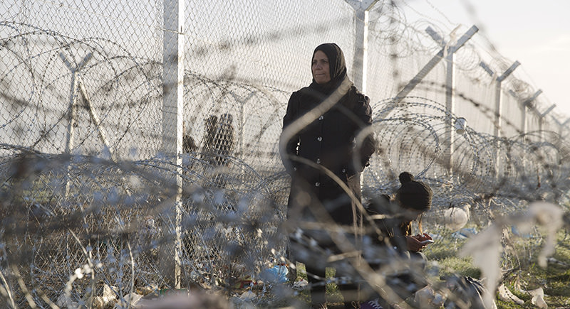 A woman stands while another crouches down to check her mobile phone near the border crossing in front to a wire fence that separates the Greek side from the Macedonian one at the northern Greek border station of Idomeni (AP Photo)