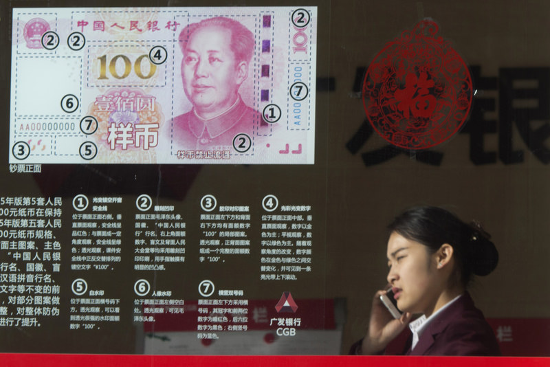 In this Feb. 16, 2016 file photo, a woman speaks on her phone near a display highlighting the new Chinese bank notes at a bank in Beijing. (AP Photo)