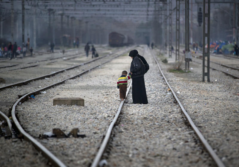 A Syrian woman holding the hand of a toddler walking on a railway track at the northern Greek border station of Idomeni.
