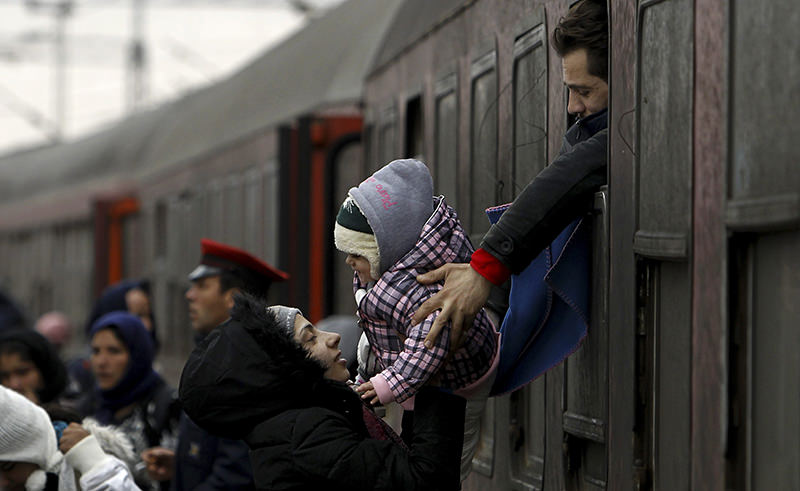 A refugee man passes a baby to a woman from a train window, upon their arrival at the transit center for refugees near northern Macedonian village of Tabanovce, Wednesday, Feb. 10, 2016 (AP Photo)
