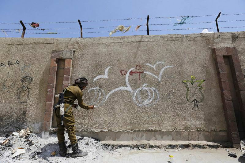 An armed Yemeni soldier paints graffiti in support of peace in the war-affected country on a wall in Sanaa. (EPA Photo)