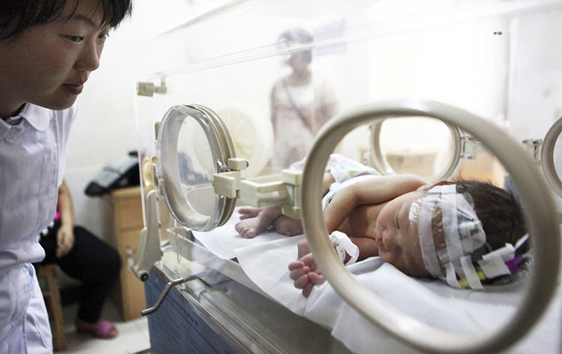 A nurse (L) looks at an abandoned newborn baby resting in an incubator after he was rescued from a sewage pipe at a hospital in Jinhua, Zhejiang province May 28, 2013.(Reuters Photo)