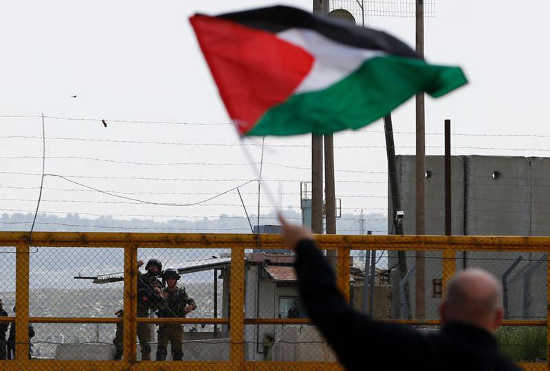 A Palestinian man waving his national flag in front of Israeli soldiers as they mark Land Day outside the compound of the Israeli-run prison in the Israeli occupied West Bank.