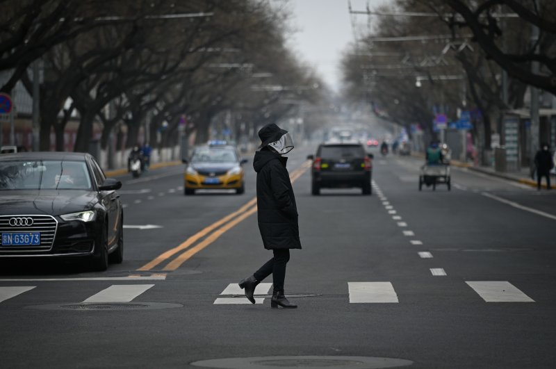 A woman wearing a face mask crosses a street in Beijing, Feb. 25, 2020. (AFP Photo)