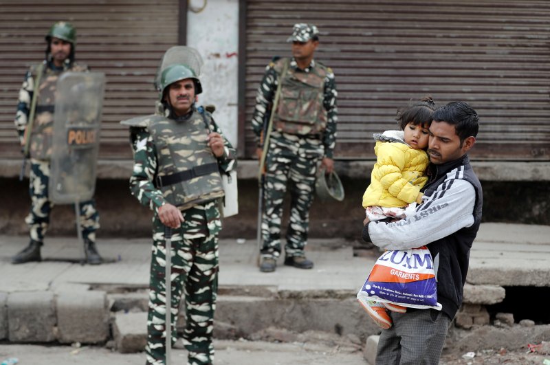 A man carrying a child walks past security forces in a riot affected area following clashes between people demonstrating for and against a new citizenship law, New Delhi, Feb. 27, 2020. (REUTERS Photo)