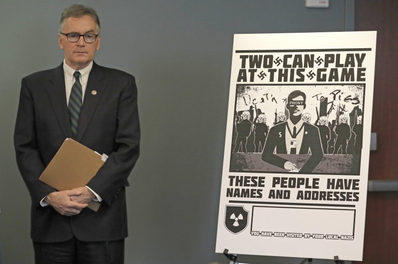 U.S. Attorney Brian Moran stands next to a poster that was mailed earlier in the year to the home of an investigative reporter, Seattle, Feb. 26, 2020. (AP Photo)