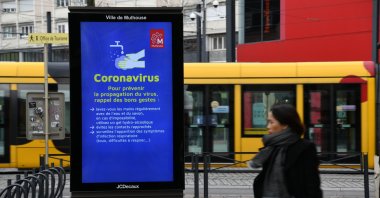 A woman walks past a screen displaying information on precautionary measures to reduce the risk of spreading COVID-19, the new coronavirus, on March 6, 2020, in Mulhouse, eastern France. (AFP Photo)