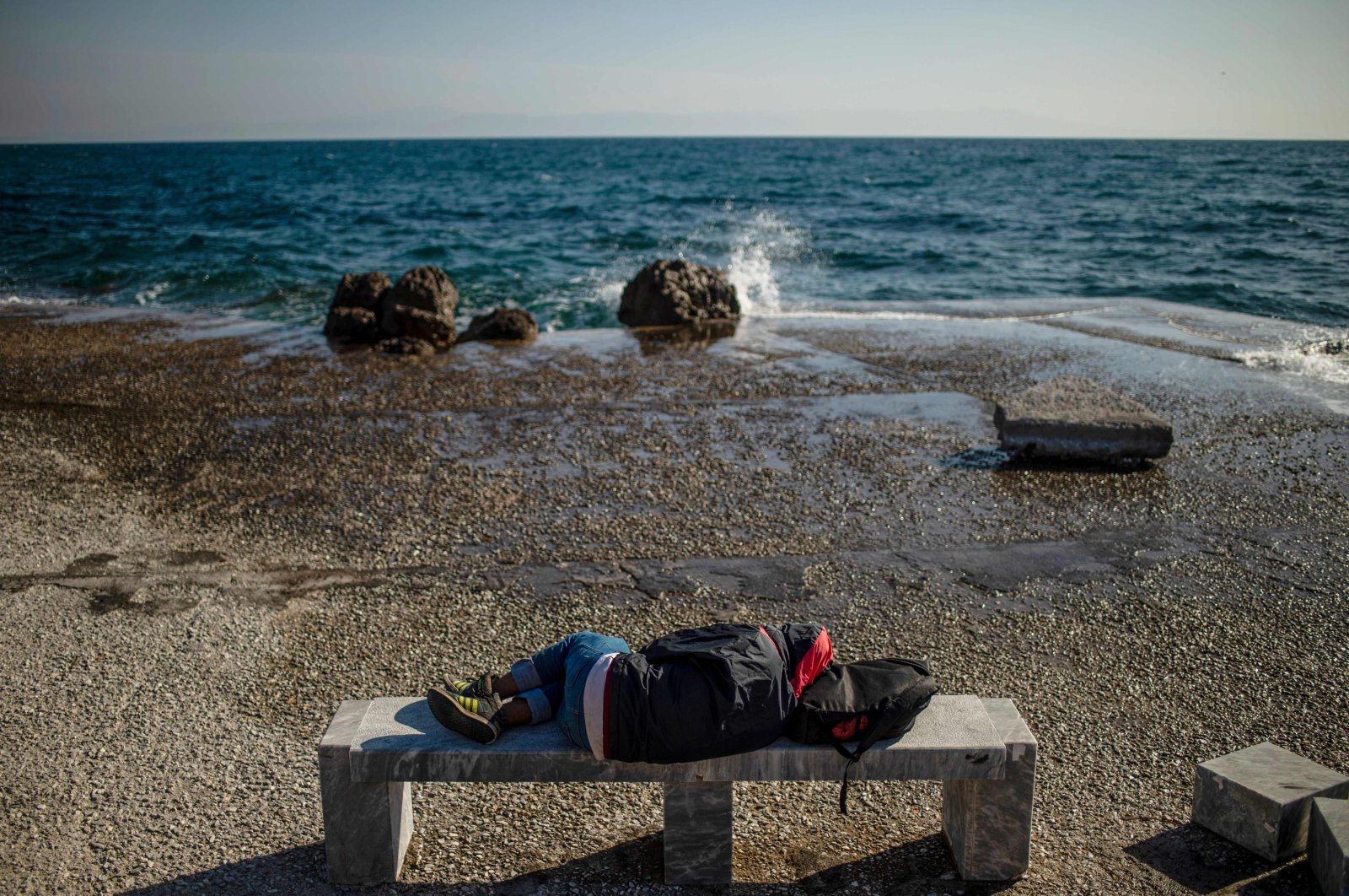 A migrant sleeps on a bench at the harbor quay on the island of Lesbos, Greece, on March 3, 2020 (AFP Photo)