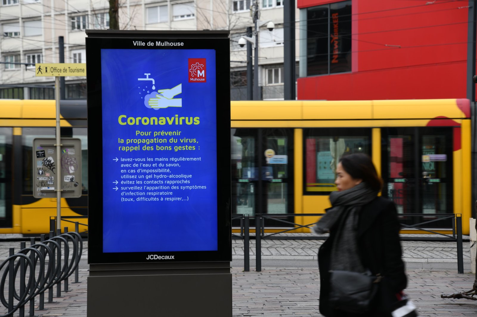 A woman walks past a screen displaying information on precautionary measures to reduce the risk of spreading COVID-19, the new coronavirus, on March 6, 2020, in Mulhouse, eastern France. (AFP Photo)