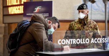 A passenger leaving from Milan Central railway station signs a release form next to a patrolling soldier, Milan, March 9, 2020. (AP Photo)