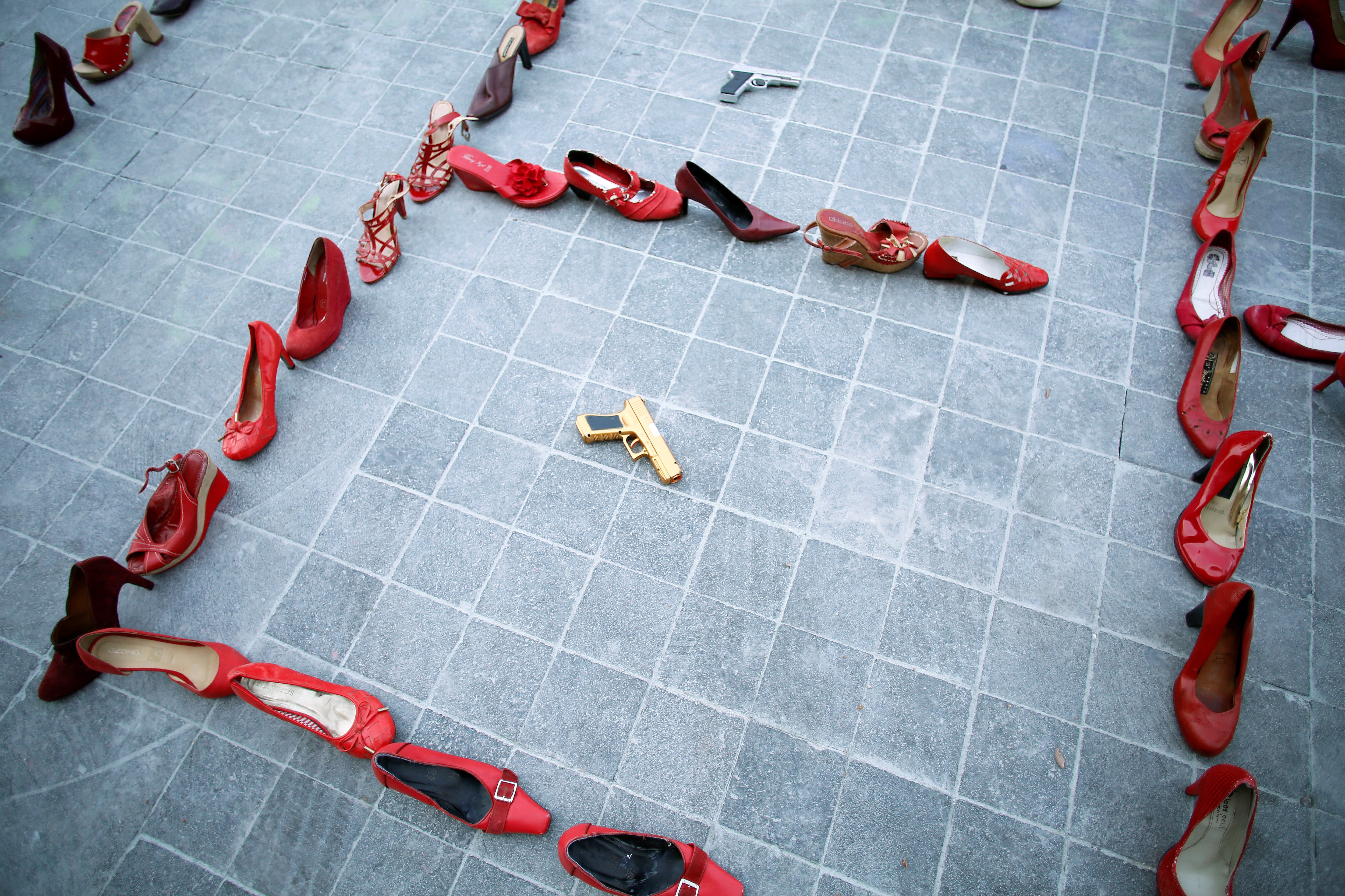 Pairs of women's red shoes are displayed next to a toy gun during the 