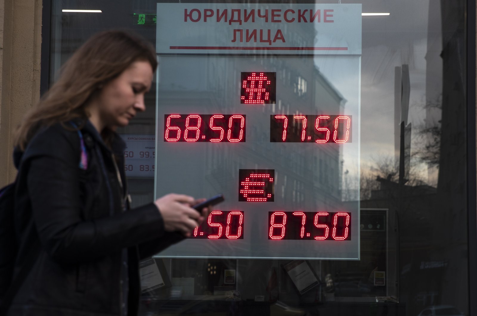 A woman walks past an currency exchange office screen displaying the exchange rates of U.S. Dollar and Euro to Russian Rubles, in Moscow, Russia, Monday, March 9, 2020. (AP Photo)