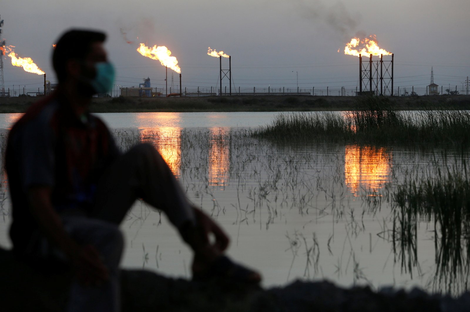 Flames emerge from flare stacks at Nahr Bin Umar oil field, as a man is seen wearing a protective face mask following the outbreak of the coronavirus, north of Basra, Iraq, March 9, 2020. (Reuters Photo)
