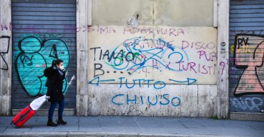 A commuter wearing a protective mask walks past closed shops and an inscription on the wall reading "All Closed," Rome, March 11, 2020. (AFP Photo)