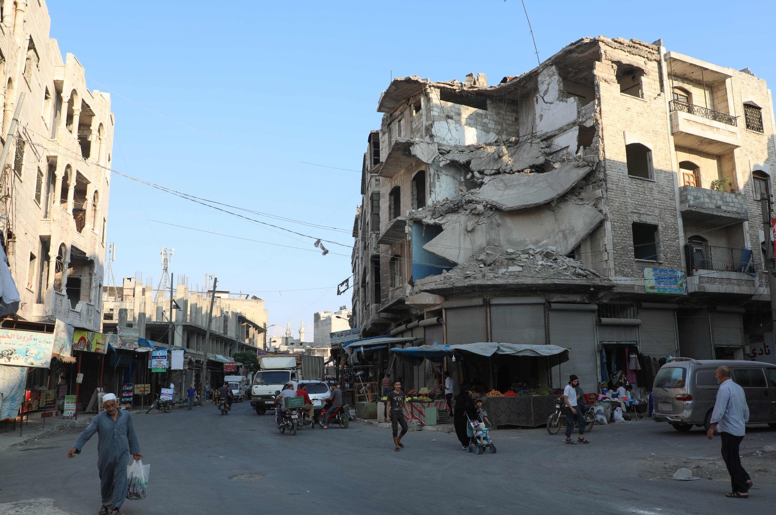 People walk near heavily damaged buildings due to the Syrian regime's attacks in the opposition-held city of Idlib in northwestern Syria on September 16, 2019. (AFP Photo)