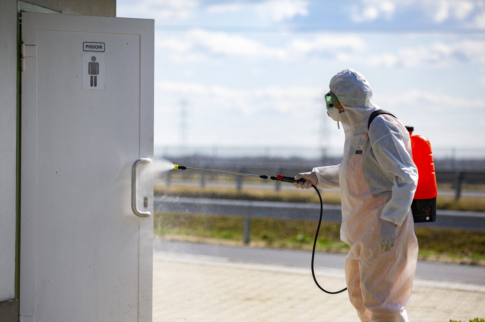 An employee of the national public road maintenance company sprays a public restroom door with disinfectant to prevent the spread of the new coronavirus at a rest area of the M70 motorway near Csornyefold, March 10, 2020. (AP Photo)