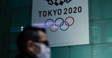 A man wearing a protective face mask walks past a banner for Tokyo 2020 Olympics in Tokyo, March 11, 2020. (Reuters Photo)