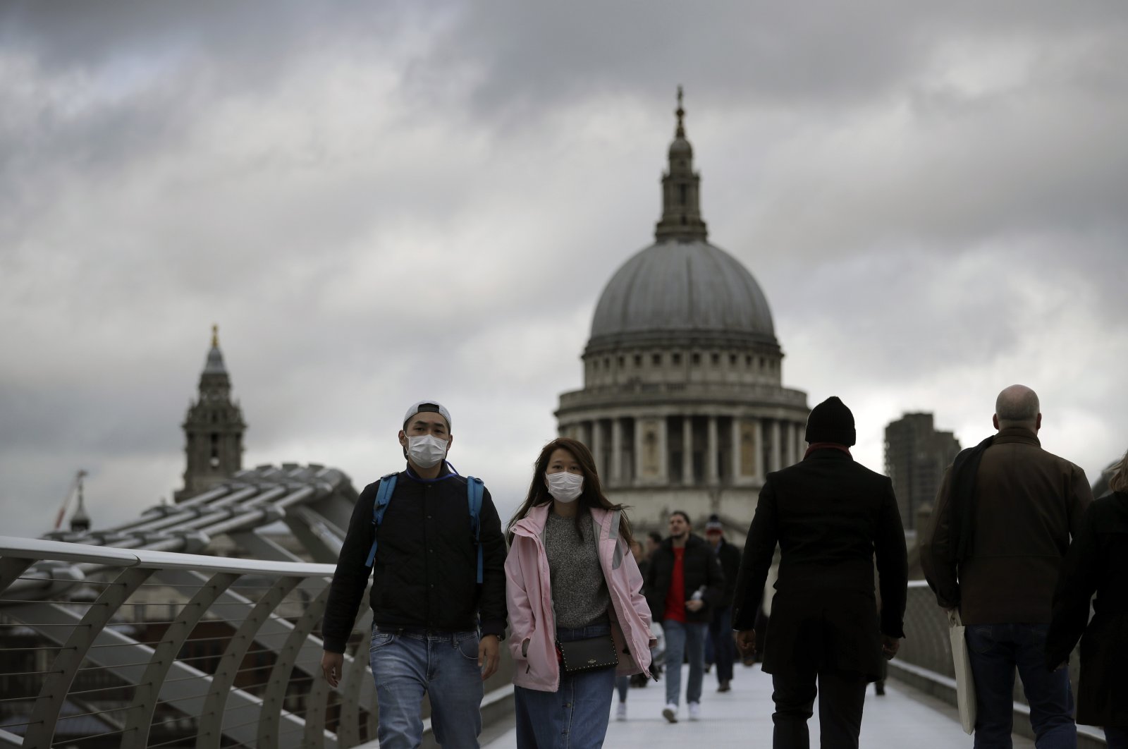 People wearing face masks walk across the Millennium footbridge backdropped by the dome of St. Paul's Cathedral in London, Tuesday, March 10, 2020. (AP Photo)