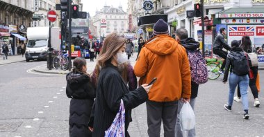 A woman looks at her phone as she wears a face mask, Leicester Square, London, March 13, 2020. (AP Photo)