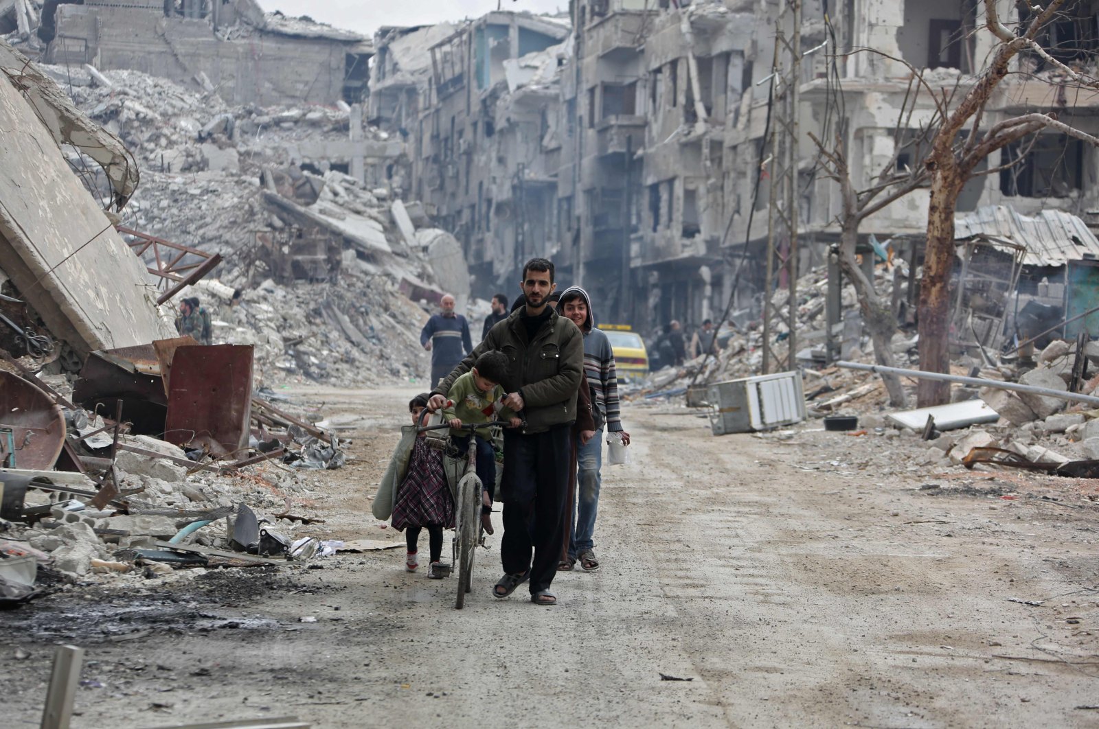 In this file photo taken on March 30, 2018, civilians walk in a destroyed neighborhood in the former opposition-held town of Harasta in eastern Ghouta, a week after regime forces retook the town from the opposition. (AFP Photo)