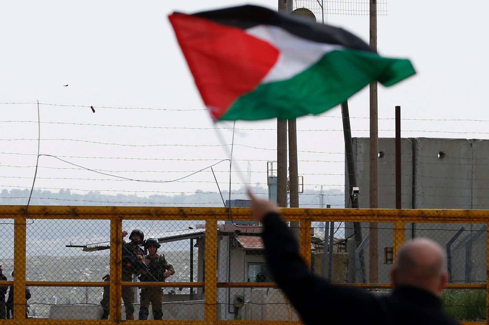 A Palestinian protester waves his national flag in front of Israeli security forces outside the compound of the Israeli-run Ofer prison near Betunia in the Israeli-occupied West Bank, March 30, 2016. (AFP Photo)