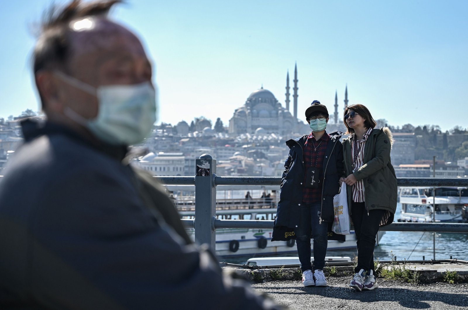 Tourists wearing face masks sit and stand on Galata Bridge in Istanbul, on March 13, 2020, amid the outbreak of COVID-19, the new coronavirus. (AFP Photo)