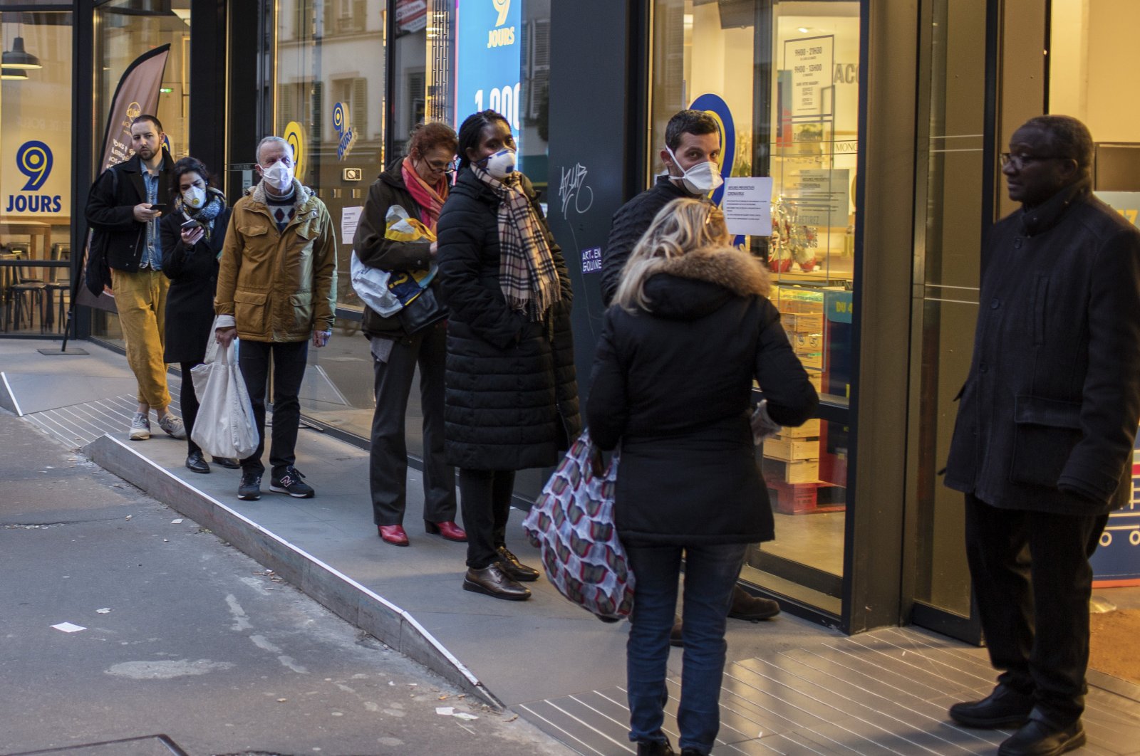 People wearing protective masks line up using social distancing to queue at a supermarket in Paris, Monday, March 16, 2020. (AP Photo)