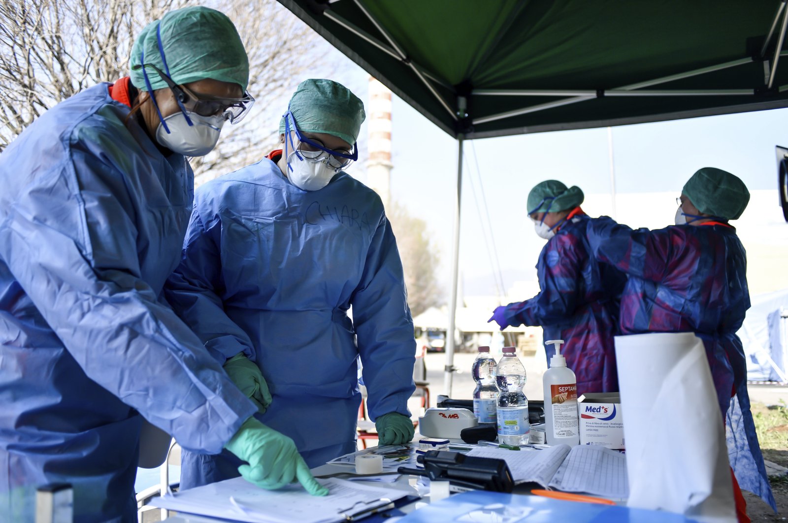 Medical personnel help each other to dress, in background, as others check papers at an emergency tent set up outside the hospital for first evaluation, in Brescia, Northern Italy, Tuesday, March 17, 2020. (LaPresse via AP)