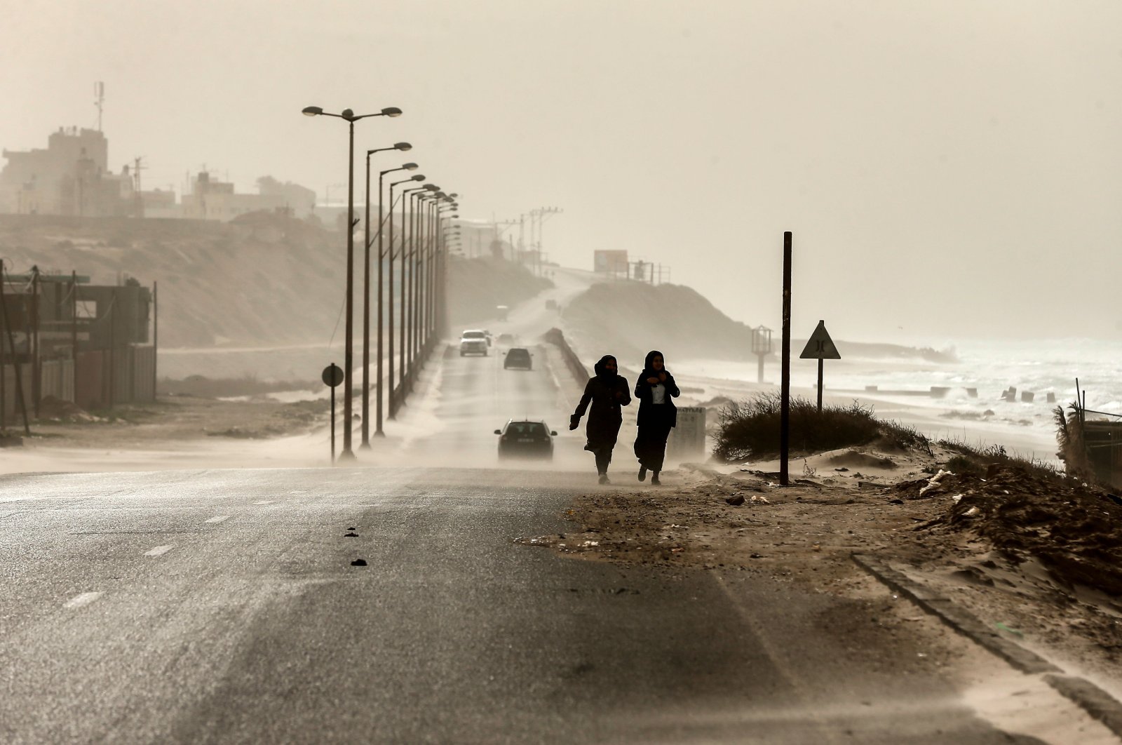 Two women walk along the sea front as heavy winds blow dust and sand across a main road in occupied Gaza City, Jan. 6, 2019. (AFP Photo)