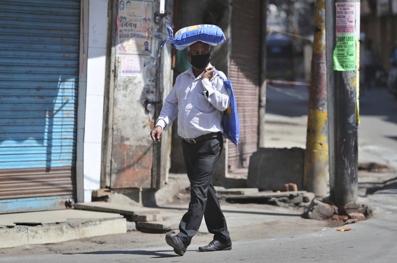 An Indian man, wearing a protective mask as a precaution against coronavirus, carries a bag of rice on his head during restrictions, Jammu, Friday, March 20, 2020. (AP Photo)